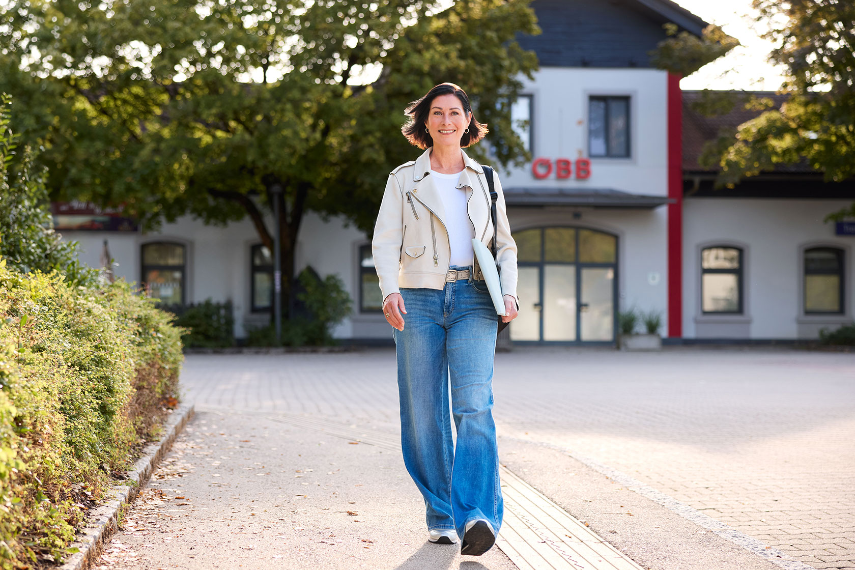Eine Frau geht mit Laptop und Rucksack in die Arbeit, im Hintergrund ist ein ÖBB Bahnhof.