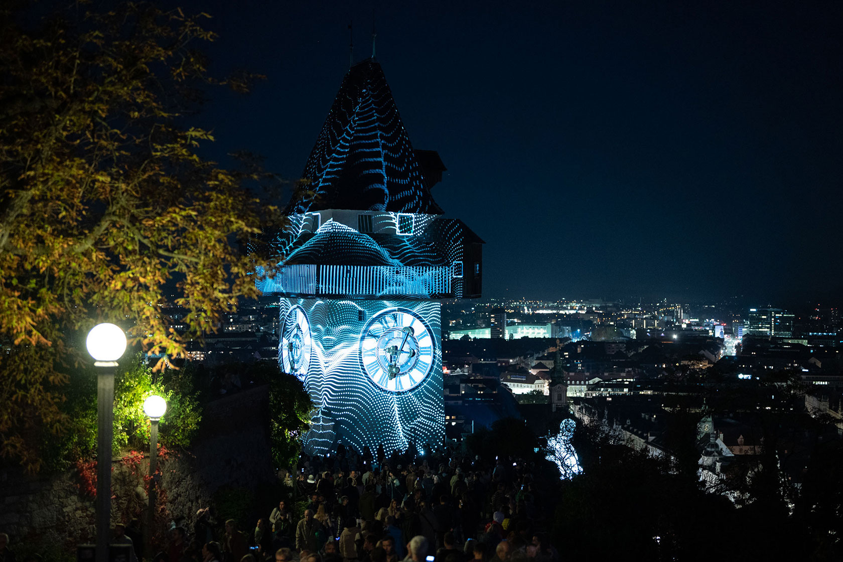 Ein Uhrturm bei Nacht, über den eine Lichtprojektion geblendet wird.