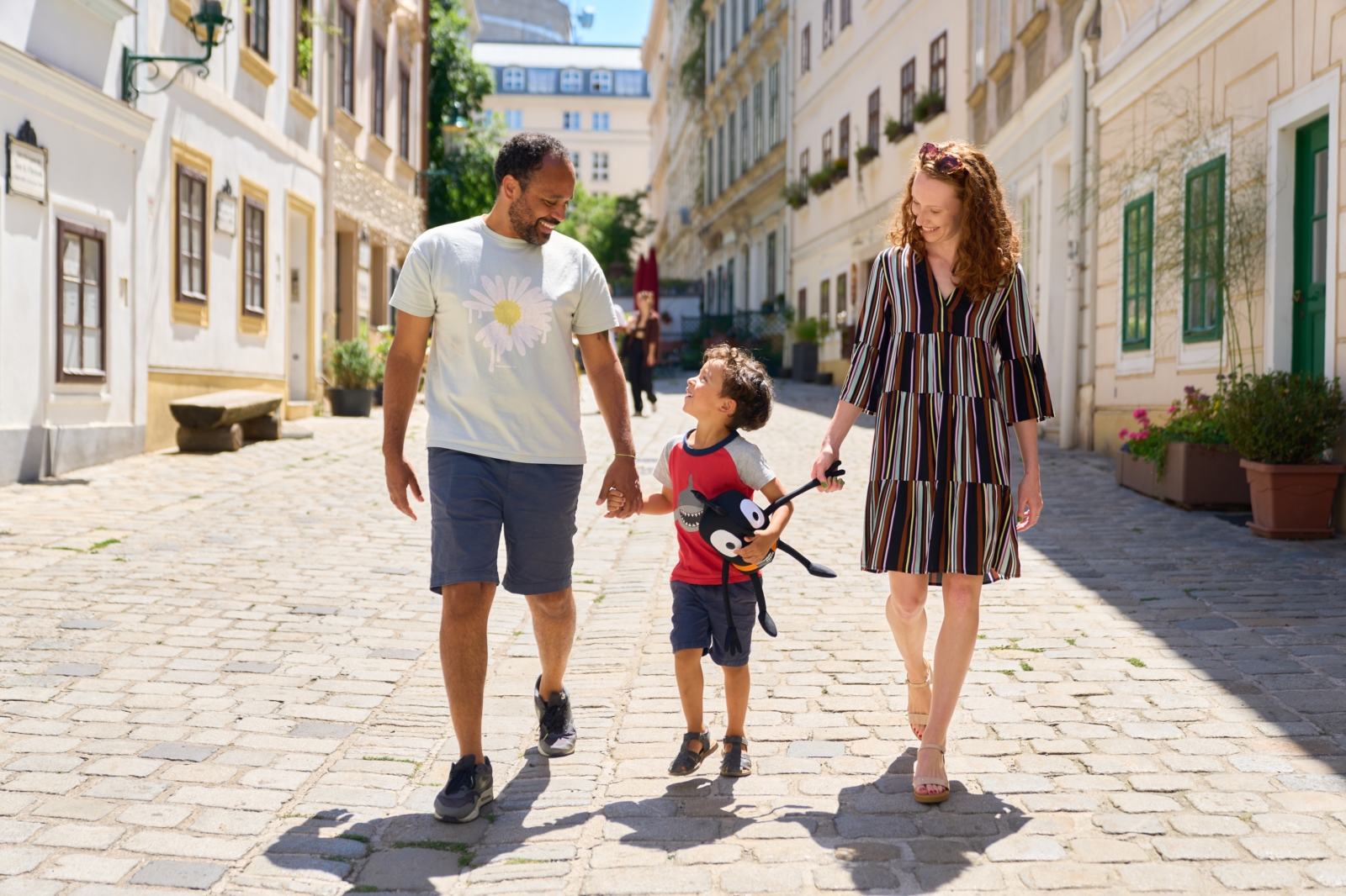Mann und Frau mit Kind in der Mitte spazieren durch die Wiener Innenstadt.