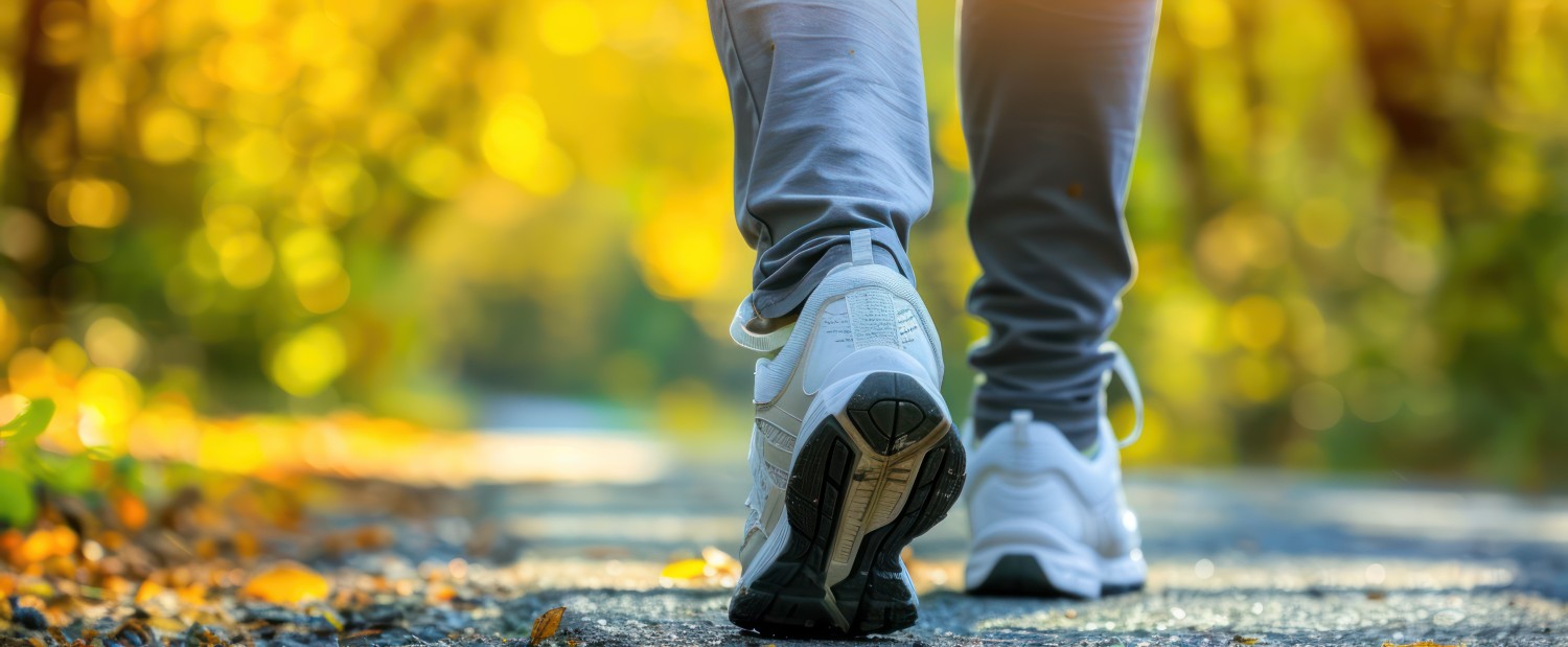 Nahaufnahme von Füßen in Sportschuhen, die über einen Herbstboden gehen.