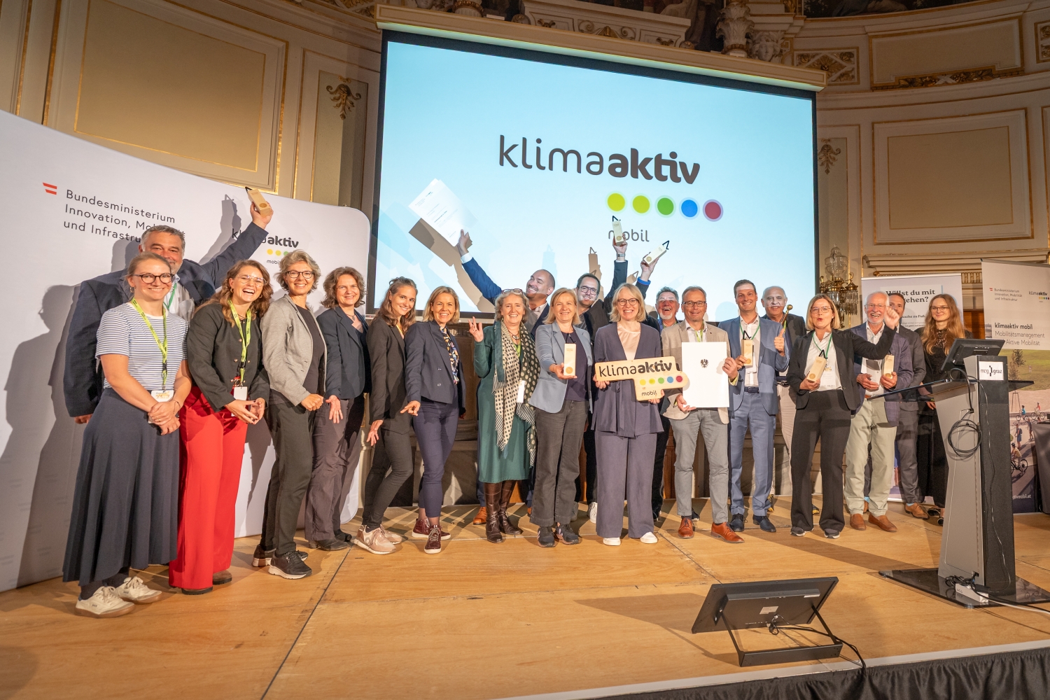 alle Gewinner:innen auf einem gemeinsamen Bild - Sie halten die Trophäen und Urkunden in die höhe