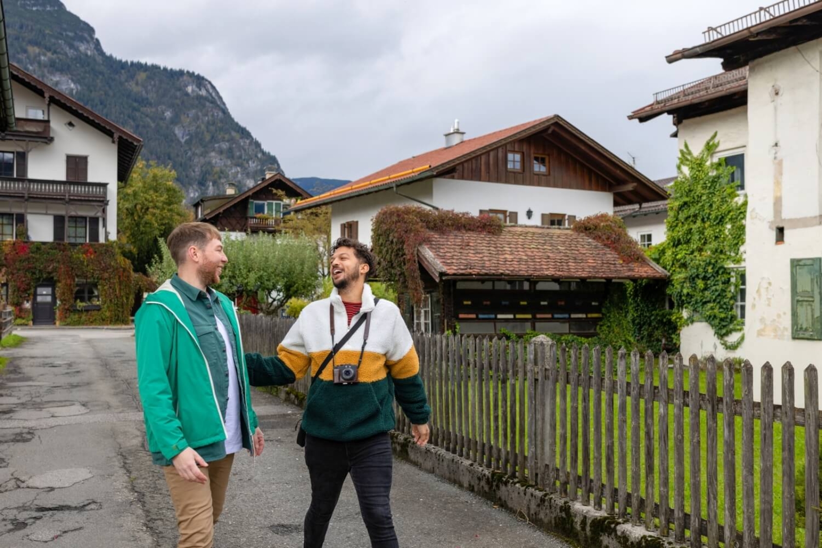 Zwei junge Männer gehen durch ein Dorf, im Hintergrund typisch tirolerische Häuser