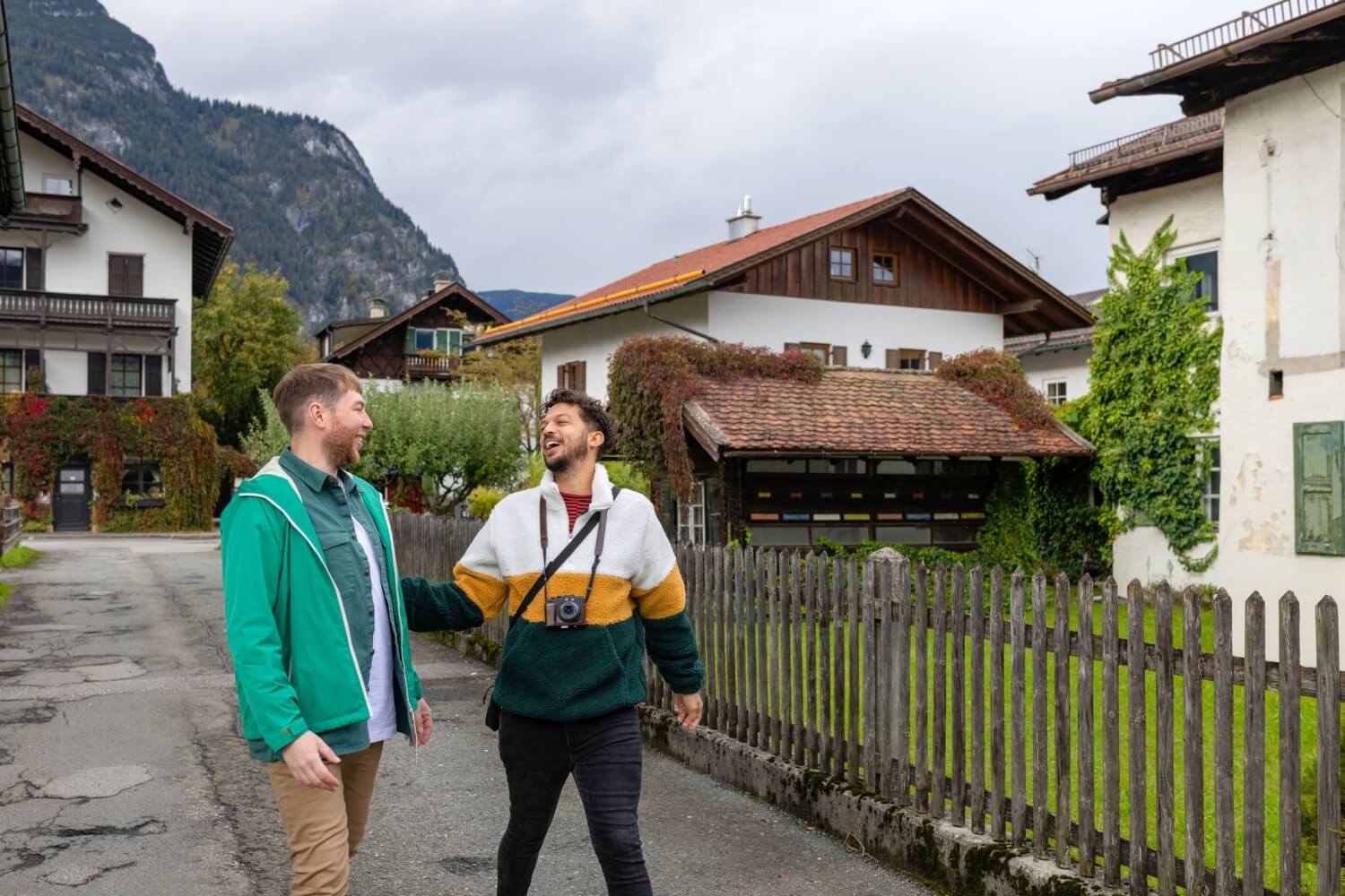 Zwei junge Männer gehen durch ein Dorf, im Hintergrund typisch tirolerische Häuser