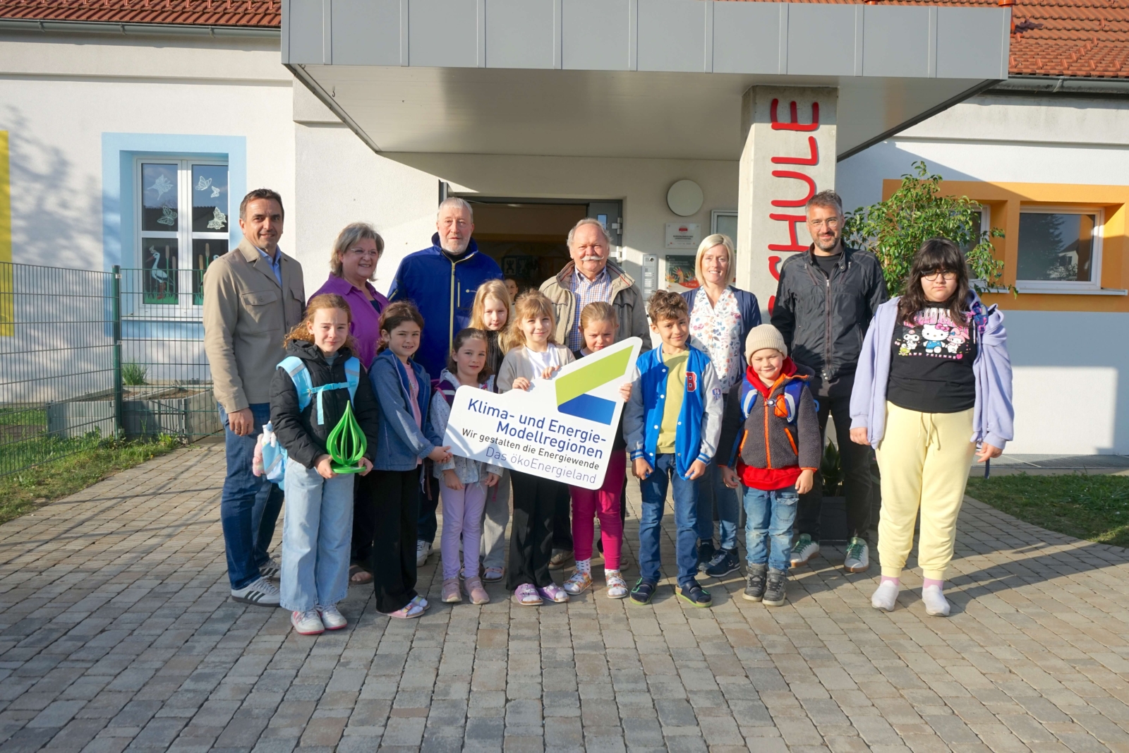 Eine Gurppe von Kindern und erwachsenen posiert für ein Bild, sie halten ein Schild der 